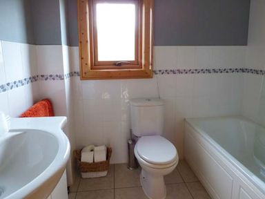 A bathroom with a toilet sink bathtub window and basket with toilet paper at Ty Pren in Llanrhian near St Davids