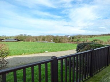 A view of a grassy field with bushes and trees seen from a wooden balcony at Ty Pren in Llanrhian near St Davids