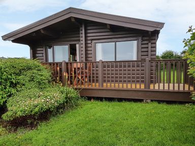 A wooden cabin with a porch and garden plants at Ty Pren in Llanrhian near St Davids