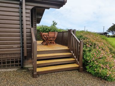 An outdoor wooden deck with stairs and a table with chairs beside a garden at Ty Pren in Llanrhian near St Davids