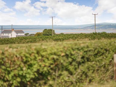 A landscape with green hedges a house and telephone poles with hills and water in the background at The Dairy in Penuel near Llanmorlais