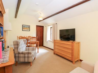 A living room with a plaid armchair wooden dining table wooden chest of drawers and a television at Moonlight Cottage in Coltishall
