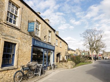 A stone building with a bakery called Bakery On The Water and a bicycle outside on a street with other stone buildings