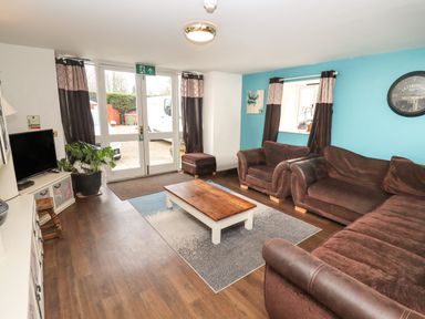 A living room with brown sofas a wooden coffee table and double glass doors at Greyhound Barn Barnsley near Cirencester