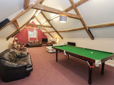A game room with a billiard table and multiple sofas under exposed wooden beams at Greyhound Barn Barnsley near Cirencester