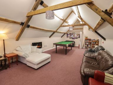 A game room with a pool table two sofas bookshelf and exposed wooden beams at Greyhound Barn Barnsley near Cirencester