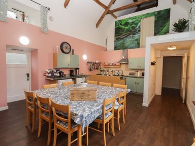 A kitchen and dining area with wooden chairs around a table covered with a cloth at Greyhound Barn Barnsley near Cirencester