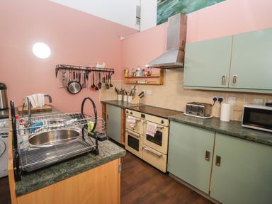 A kitchen with a stove sink toaster microwave and utensils hanging on a pink wall at Greyhound Barn in Barnsley near Cirencester