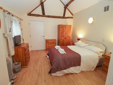 A bedroom with a double bed with folded towels bedside tables a wooden wardrobe and drawers at Greyhound Barn Barnsley near Cirencester
