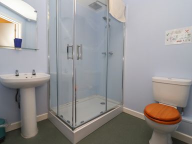 A bathroom with a shower enclosure a pedestal sink and a toilet with a wooden seat at Greyhound Barn in Barnsley near Cirencester