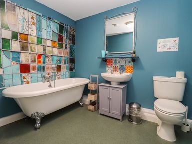 A bathroom with a clawfoot bathtub sink with a mirror and cabinet toilet and colorful tiled wall at Greyhound Barn Barnsley near Cirencester