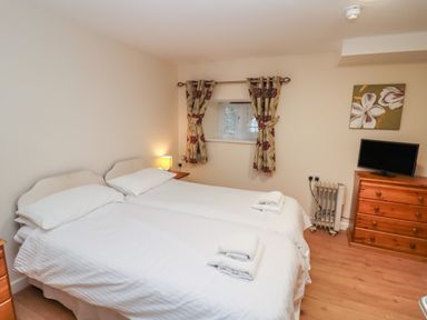 A bedroom with two single beds a wooden dresser a small television and floral curtains at Greyhound Barn Barnsley near Cirencester