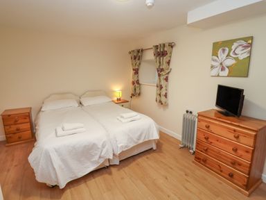 A bedroom with two single beds joined together bedside tables a wooden dresser with a television and floral curtains at Greyhound Barn in Barnsley near Cirencester
