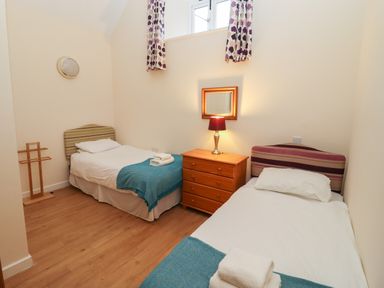A bedroom with two single beds, a wooden dresser with a lamp and mirror, and patterned curtains at Greyhound Barn in Barnsley near Cirencester