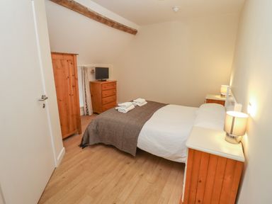 A bedroom with a bed side tables with lamps a wardrobe and a chest of drawers with a tv at Greyhound Barn in Barnsley near Cirencester