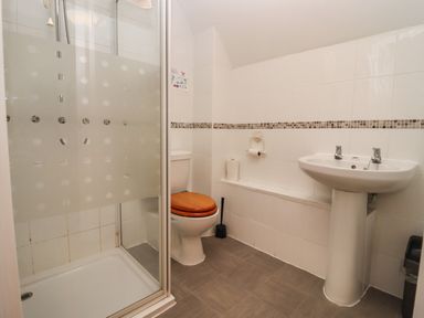 A bathroom with a shower enclosure a toilet with wooden seat a pedestal sink and tiled walls at Greyhound Barn Barnsley near Cirencester