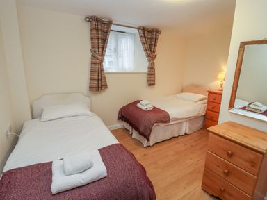 A bedroom with two single beds a wooden dresser a chest of drawers with a lamp and a small window with curtains at Greyhound Barn in Barnsley near Cirencester