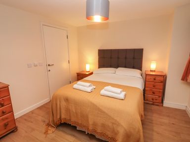 A bedroom with a double bed covered with a yellow blanket and white towels on top two wooden bedside tables with lamps Greyhound Barn Barnsley near Cirencester