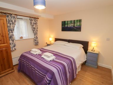 A bedroom with a double bed two bedside tables lamps wooden wardrobe and a window with flowered curtains at Greyhound Barn Barnsley near Cirencester