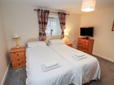 A bedroom with two single beds two nightstands with lamps a chest of drawers with a TV and a window with curtains at Greyhound Barn in Barnsley near Cirencester