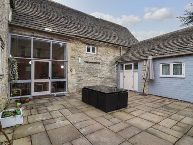 An outdoor paved courtyard with patio furniture and a closed umbrella at Greyhound Barn Barnsley near Cirencester