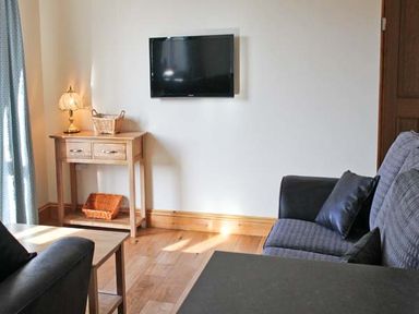 A living room with a wall mounted TV a wooden side table with baskets a lamp and two sofas at Moat Farm Cottage in Wood Dalling