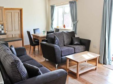 A living room with sofas a wooden coffee table and a dining table with chairs at Moat Farm Cottage in Wood Dalling