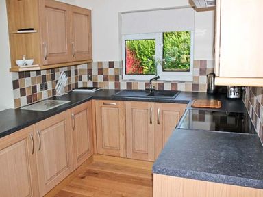 A kitchen with wooden cabinets black countertops a window and tiled backsplash at Moat Farm Cottage in Wood Dalling
