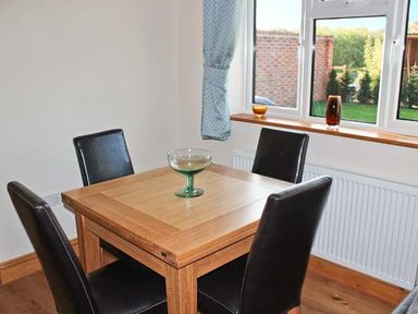 A dining area with a wooden square table and four black chairs near a window with blue curtains at Moat Farm Cottage in Wood Dalling