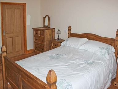A bedroom with a wooden bed with white bedding a wooden dresser with a mirror and a wooden nightstand with a lamp at Moat Farm Cottage Wood Dalling