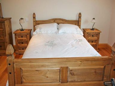 A bedroom with a wooden double bed white bedding two bedside tables with lamps and wooden floor at Moat Farm Cottage in Wood Dalling