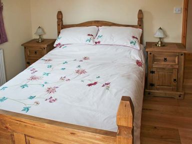 A bedroom with a wooden bed with floral bedding and two wooden nightstands with lamps at Moat Farm Cottage in Wood Dalling