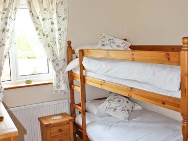 A bedroom with a wooden bunk bed next to a window with floral curtains at Moat Farm Cottage in Wood Dalling