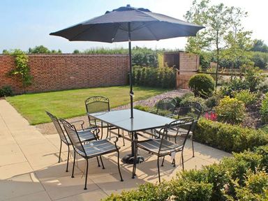 An outdoor patio with a table and six chairs under a large umbrella at Moat Farm Cottage in Wood Dalling