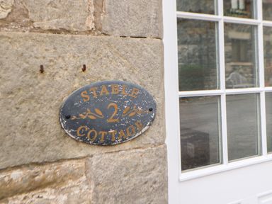 A close up of a sign on a stone wall next to a white window at Stable Cottage in Belford near Bamburgh
