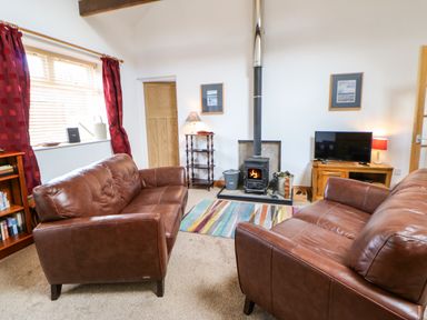 A living room with two brown leather sofas a wood burning stove colorful rug and a television at Stable Cottage Belford near Bamburgh