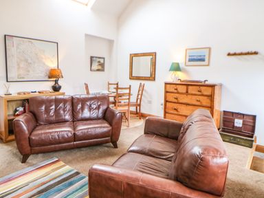 A living room with two brown leather sofas a striped rug a wooden dresser and a dining table at Stable Cottage in Belford near Bamburgh