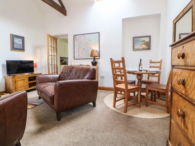 A living room with brown leather sofas a wooden dining table with chairs a television and framed pictures on walls at Stable Cottage in Belford near Bamburgh