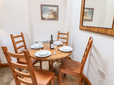 A dining area with a round wooden table set for four with white plates bowls wine glasses and a bottle at Stable Cottage in Belford near Bamburgh