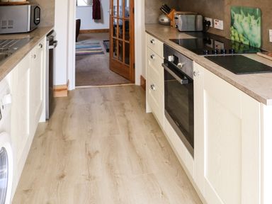 A kitchen with wooden flooring and beige cabinets with a built-in oven a toaster and a microwave at Stable Cottage in Belford near Bamburgh