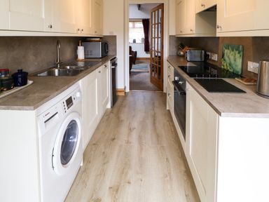 A kitchen with white cabinets a washing machine microwave toaster and kettle at Stable Cottage Belford near Bamburgh