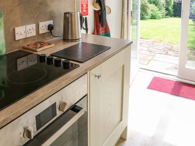A kitchen counter with stovetop oven a kettle and an open door leading to a garden at Stable Cottage Belford near Bamburgh