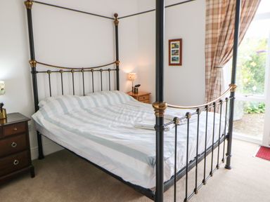 A bedroom with a four-poster bed bedside tables with lamps framed pictures and a window with curtains at Stable Cottage in Belford near Bamburgh