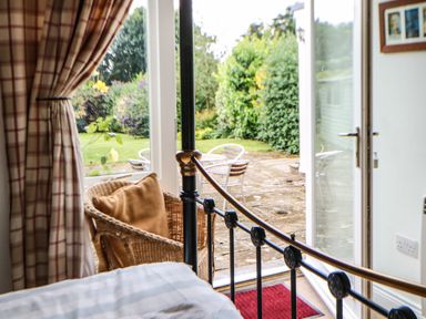 A bedroom with wicker chair and metal bed frame next to open door leading to garden patio at Stable Cottage Belford near Bamburgh