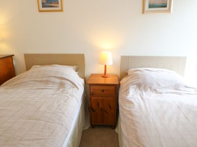 A bedroom with two single beds separated by a wooden nightstand with a lamp at Stable Cottage in Belford near Bamburgh