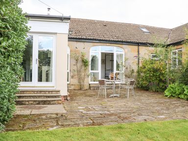 A stone patio with metal table and chairs outside a house with large windows and plants at Stable Cottage in Belford near Bamburgh