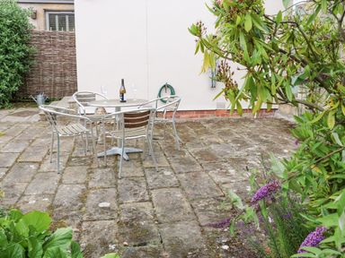 An outdoor patio with a round table and four metal chairs a bottle and two glasses on the table plants and greenery surrounding the patio at Stable Cottage Belford near Bamburgh