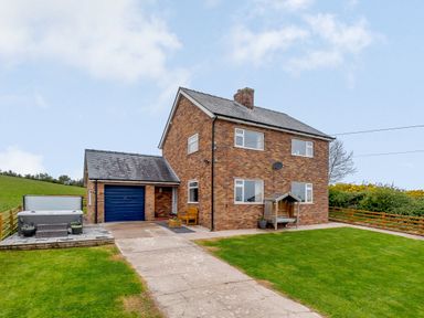 A brick house with a driveway garage and a wooden bench near the entrance at Pen Y Gaer in Llannefydd near Abergele and Denbigh