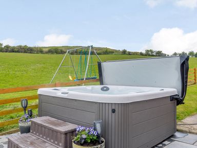 An outdoor hot tub with steps and flower pots next to a swing set in a grassy field at Pen Y Gaer in Llannefydd near Abergele and Denbigh