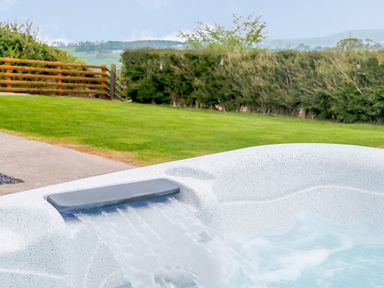 A hot tub with water flowing into it in a garden with grass and hedges at Pen Y Gaer in Llannefydd near Abergele and Denbigh